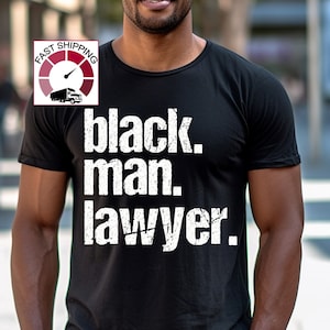 May include: Black t-shirt with the text "black. man. lawyer." in white distressed lettering.