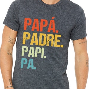 May include: A dark heather grey t-shirt with a vintage-style graphic that reads "PAPÁ. PADRE. PAPI! PA."