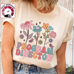 May include: A cream-colored t-shirt with a floral design and the text "PROGRAM DIRECTOR" in colorful, retro-style letters.