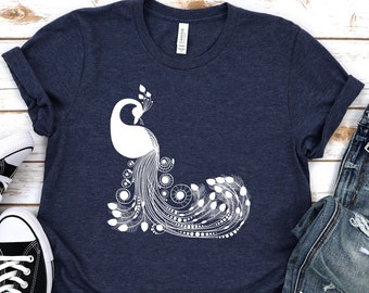 May include: A navy blue t-shirt with a white graphic of a peacock with its tail feathers spread out. The shirt is laid out on a white wooden surface with a pair of black canvas shoes and a pair of blue jeans.