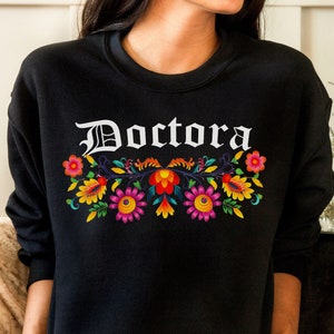 May include: Black sweatshirt with the word "Doctora" in white gothic lettering and a colorful floral design.