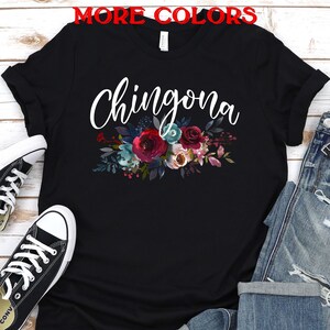 May include: Black t-shirt with the word "Chingona" in white script and a floral design in shades of red, pink, blue, and green.