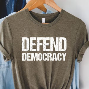 May include: A green t-shirt with the text "DEFEND DEMOCRACY" printed in white on the front.