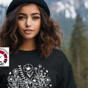 May include: Black sweatshirt with a white design of an open book with flowers growing out of it. The text "CHAPTER 70" is below the book.