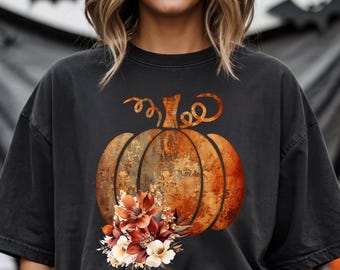 May include: Black t-shirt featuring a large, detailed pumpkin graphic with floral accents. The pumpkin is a warm orange color with a textured appearance, and the flowers are in shades of red, orange, and cream. The shirt is a comfortable, casual style.