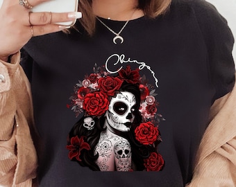 May include: Black t-shirt with a graphic of a woman with a sugar skull face surrounded by red roses and the word "Chingona" written in cursive.