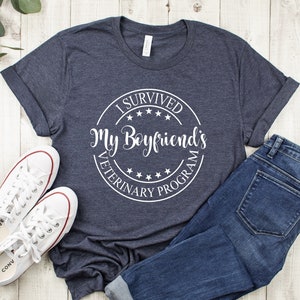 May include: A navy blue t-shirt with a white circle graphic that says "I Survived My Boyfriend's Veterinary Program".