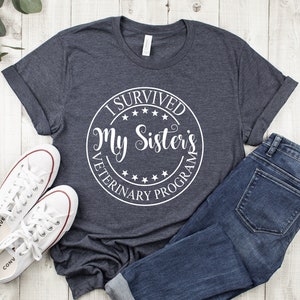 May include: A dark gray t-shirt with a white circle graphic that says "I Survived My Sister's Veterinary Program".