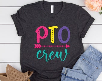 May include: A dark grey t-shirt with the text "PTO crew" in colourful letters. The letters are outlined in white and have white polka dots. There is a colourful arrow above the text.