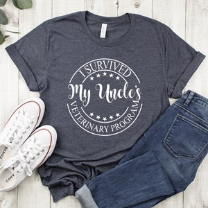 May include: A dark heather gray t-shirt with a white circle graphic that says "I Survived My Uncle's Veterinary Program".