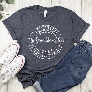 May include: A dark gray t-shirt with a white circle graphic that says "I Survived My Granddaughter's Veterinary Program".