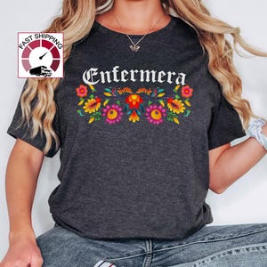 May include: A dark gray t-shirt with the word "Enfermera" in white lettering and a colorful floral design below it.