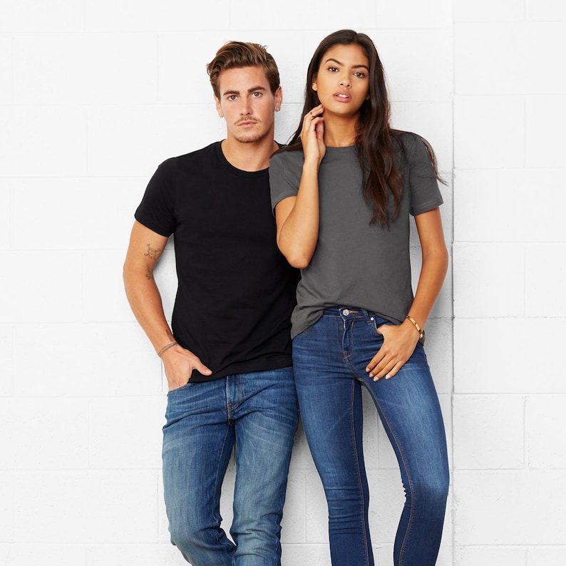 May include: Two people wearing t-shirts and jeans. The person on the left is wearing a black t-shirt and the person on the right is wearing a charcoal grey t-shirt.