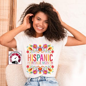May include: White t-shirt with a colorful floral design and the text "HISPANIC HERITAGE MONTH".
