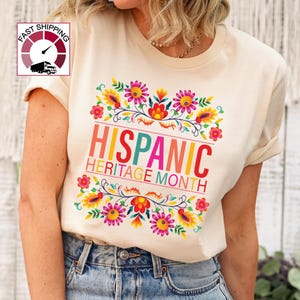 May include: A beige t-shirt with a colorful floral design and the text "Hispanic Heritage Month".