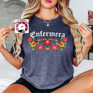 May include: A dark gray t-shirt with the word "Enfermera" in white lettering and a floral design in red, yellow, orange, and pink.