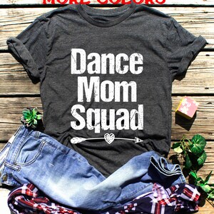May include: A dark grey t-shirt with the text "Dance Mom Squad" in white with a distressed look. A white arrow with a heart is below the text.