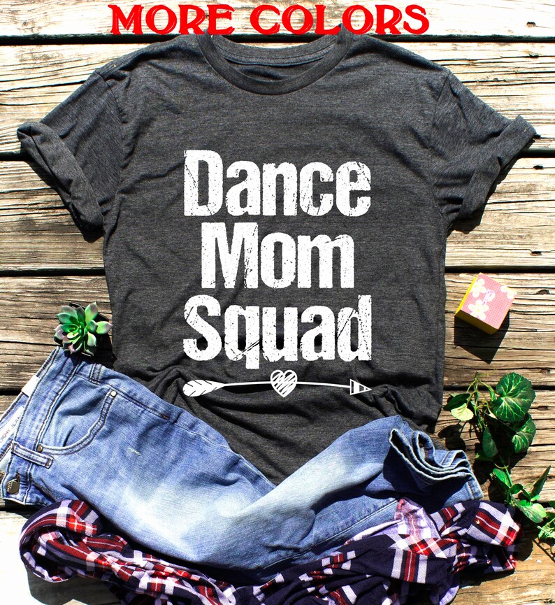 May include: A dark grey t-shirt with the text "Dance Mom Squad" in white with a distressed look. A white arrow with a heart is below the text.