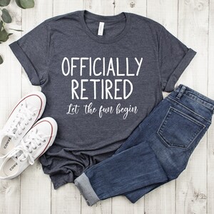 Puede incluir: Una camiseta gris oscuro jaspeada con el texto "Officially Retired Let the fun begin" en blanco.