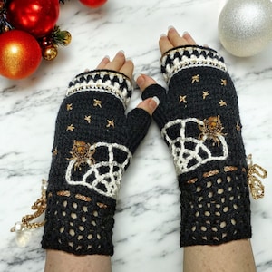 May include: A pair of black fingerless gloves with white and gold spider web designs. The gloves have a crocheted texture and are adorned with gold spider accents.