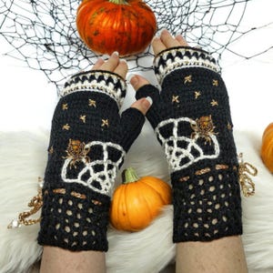 May include: Black and white crochet fingerless gloves with a Halloween theme. The gloves feature a spider and web design, gold star accents, and a decorative gold chain with pearls. The gloves are displayed with pumpkins and a spider web.