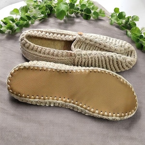 May include: A pair of beige crocheted slippers with a brown leather sole. The slippers have a simple design and are perfect for keeping your feet warm and cozy.