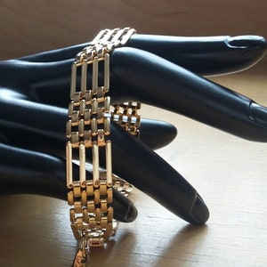 May include: A gold-toned chain bracelet with a unique, multi-layered design. The bracelet is made of linked rectangular pieces, creating a geometric pattern.