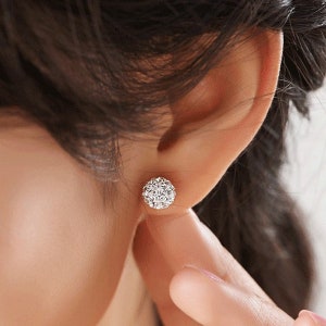 May include: A pair of silver stud earrings with a round, sparkly design. The earrings are small and delicate, and they would be a great addition to any jewellery collection.