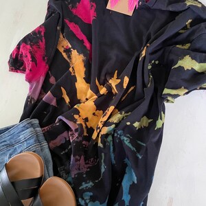 May include: A black tie-dye t-shirt with a colourful swirl pattern. The shirt is made of a soft, comfortable fabric and has a relaxed fit.