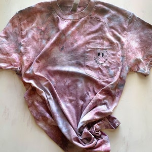 May include: A tie-dye t-shirt with a pocket featuring a smiling face and the text "Cool Moms Club".