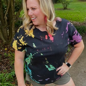 May include: A black tie-dye t-shirt with a colourful splatter pattern. The shirt has short sleeves and a relaxed fit.