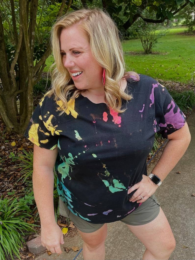 May include: A black tie-dye t-shirt with a colourful splatter pattern. The shirt has short sleeves and a relaxed fit.