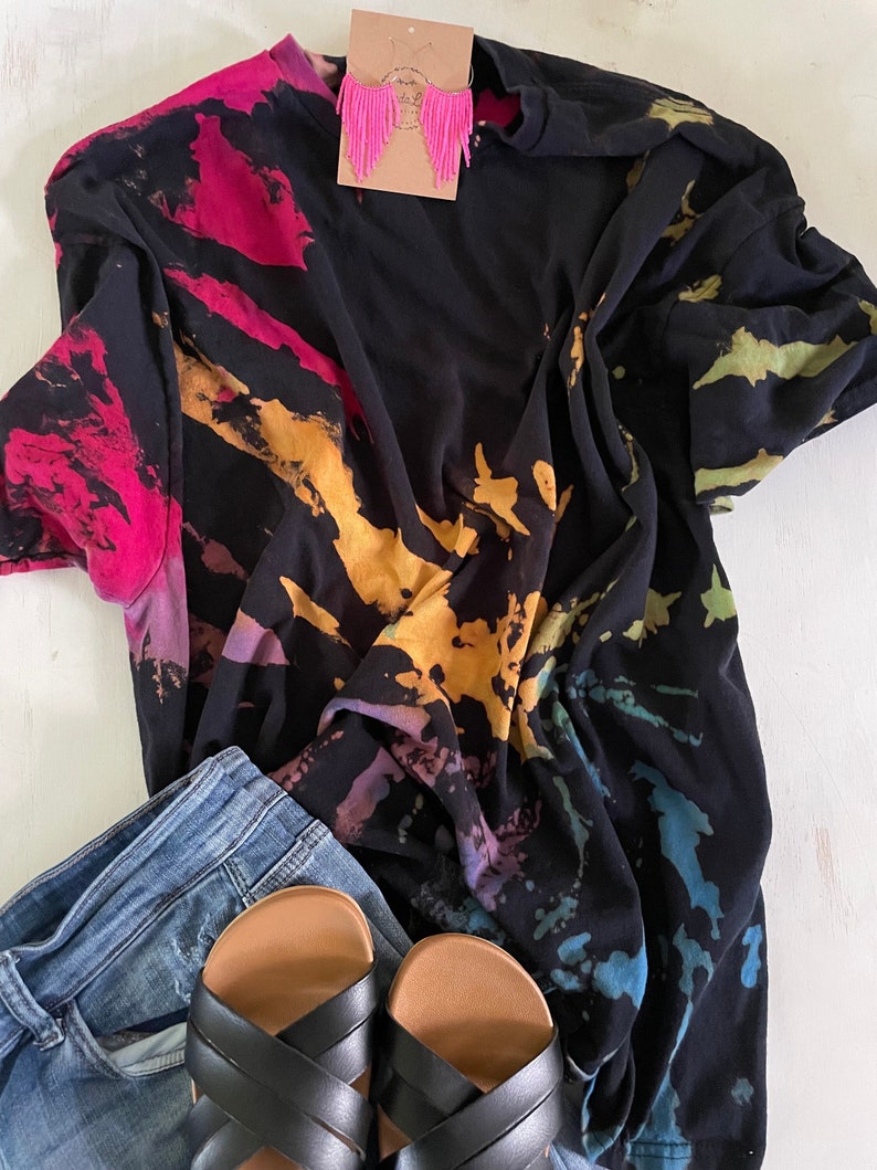 May include: A black tie-dye t-shirt with a rainbow pattern. The shirt is paired with blue jeans and black sandals.