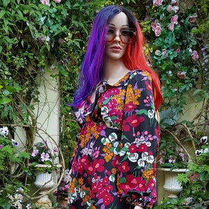 May include: A long-sleeved maxi dress with a floral print in shades of red, orange, white, and green on a black background. The dress has a V-neckline and a ruffled collar.