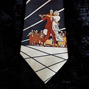 Może przedstawiać: Granatowy krawat z ukośnymi białymi paskami i zabytkową ilustracją tańczącej pary z zespołem w tle. Krawat ma kremową końcówkę z geometrycznym wzorem.