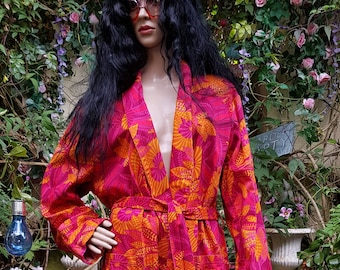 May include: A long, pink and orange floral print robe with a tie belt. The robe is worn by a mannequin with long black hair and sunglasses.