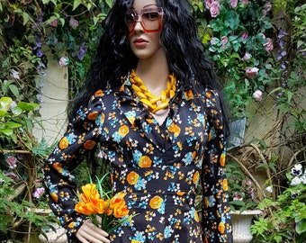 May include: A long-sleeved maxi dress with a floral print in shades of orange, blue, and white on a black background. The dress has a V-neckline and a collar. The model is wearing a yellow necklace and sunglasses.