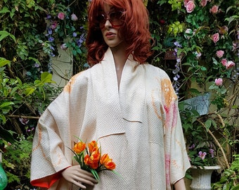 Puede incluir: Un kimono de seda blanco con un patrón floral en tonos rosa y naranja. El kimono lo lleva puesto un maniquí con el pelo rojo y gafas de sol. El maniquí está de pie en un jardín.