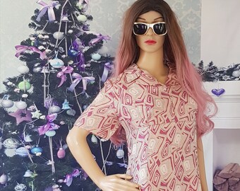 May include: A pink and beige patterned maxi dress with a short sleeve and a collared neckline. The dress is being modeled on a mannequin with pink hair and sunglasses. The mannequin is holding a gold clutch purse.