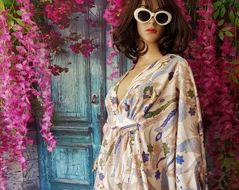 May include: A white maxi dress with a floral print featuring blue, green, and brown accents. The dress has a V-neckline and long sleeves. The model is wearing white sunglasses.