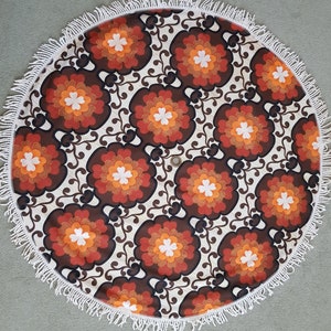 May include: A round, white, fringed tablecloth with a brown, orange, and white floral pattern.