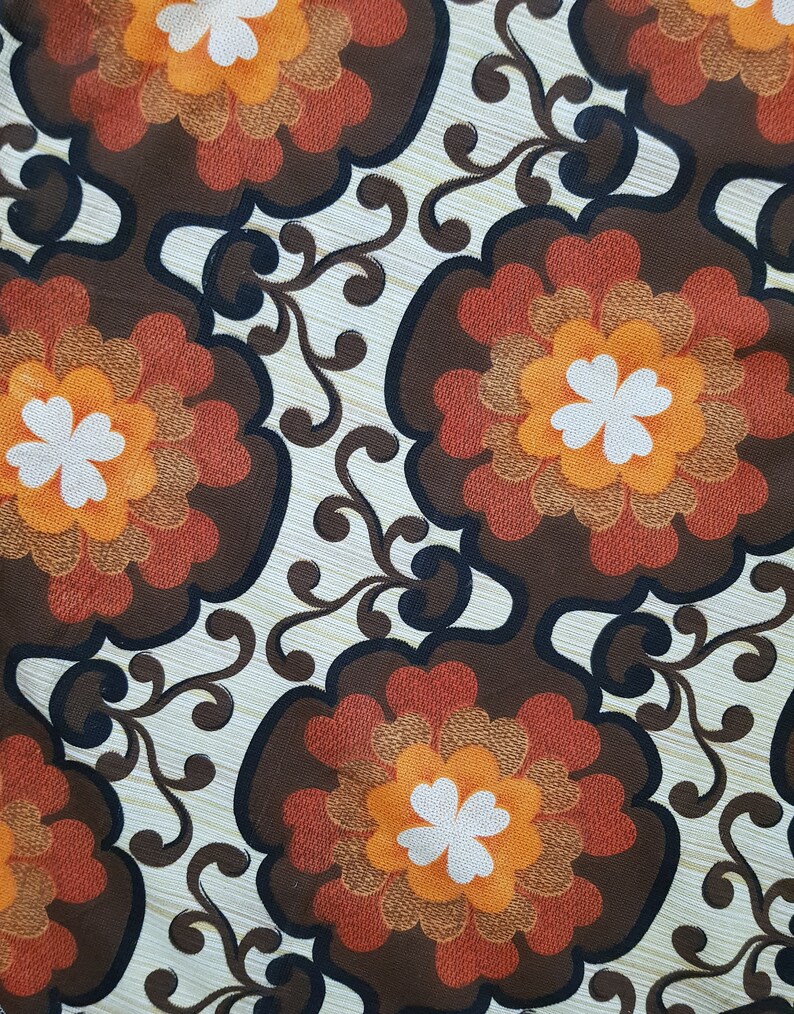 May include: A vintage fabric with a brown, orange, and white floral pattern. The fabric features a repeating design of stylized flowers with a central white clover shape.