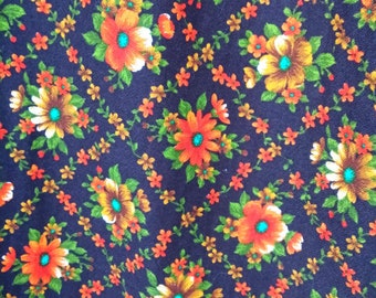 Könnte beinhalten: Ein dunkelblauer Stoff mit einem sich wiederholenden Muster aus orangefarbenen, gelben und grünen Blumen. Die Blumen haben eine braune Mitte und sind von kleinen grünen Blättern umgeben.