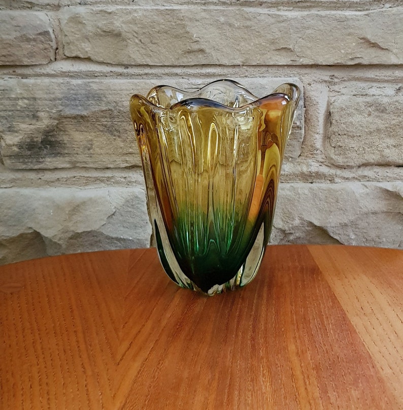 May include: A glass vase with a green and yellow swirl design. The vase has a wide mouth and a narrow base.