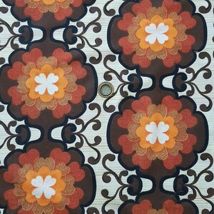 May include: A vintage fabric with a repeating pattern of brown, orange, and white flowers. The fabric has a textured background.
