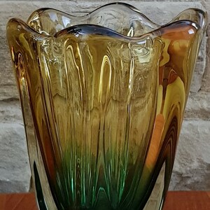 May include: A green and amber glass vase with a wavy, organic shape. The vase has a textured, rippled surface.