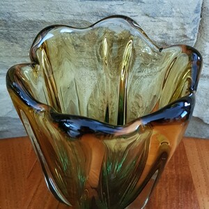 May include: A green and amber glass bowl with a wavy, organic shape. The bowl is made of thick glass and has a unique, modern design.