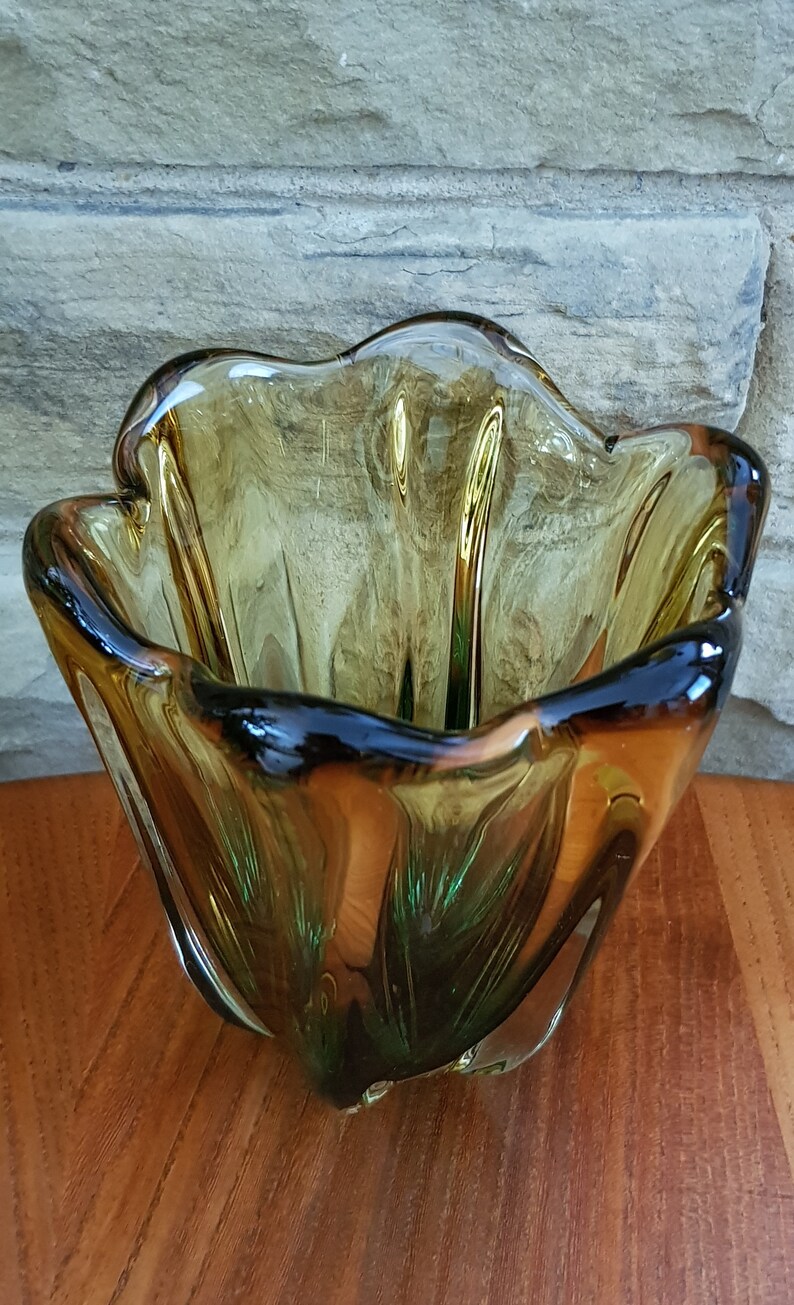 May include: A green and amber glass bowl with a wavy, organic shape. The bowl is made of thick glass and has a unique, modern design.