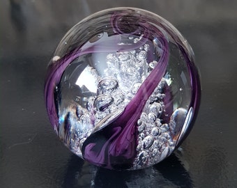 May include: A glass paperweight with a swirl of purple and silver. The paperweight is filled with small air bubbles.