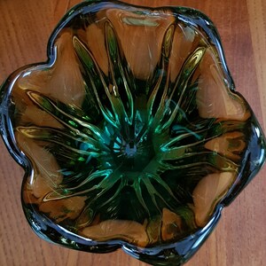 May include: A green and brown glass bowl with a flower-like design. The bowl has a deep center and a wide, flared rim.